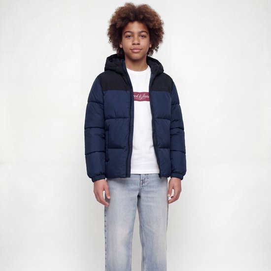 Model met krullend haar draagt een marineblauwe en zwarte pufferjas over een wit 'Jack & Jones' T-shirt en spijkerbroek.