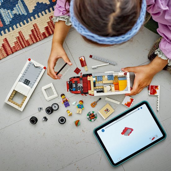 Kind bouwt LEGO camper met tablet. De camper is rood, wit en grijs met een gedetailleerd interieur.