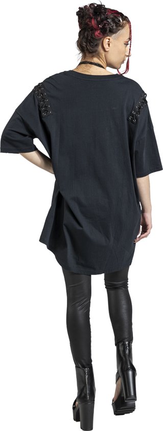 Model draagt een zwart oversized T-shirt met vetersluiting op de schouders, gecombineerd met een zwarte legging.