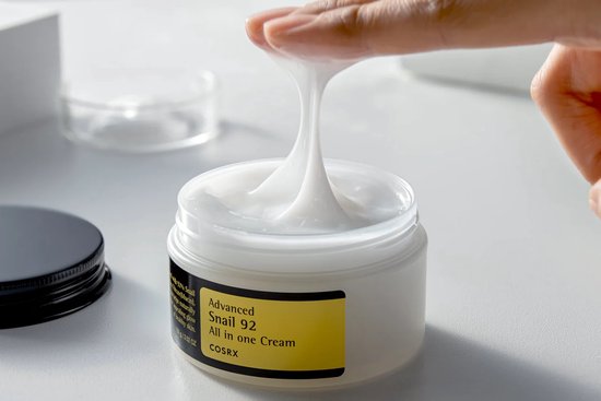 Hand haalt een klodder witte crème uit een potje, de crème is dik en draderig.