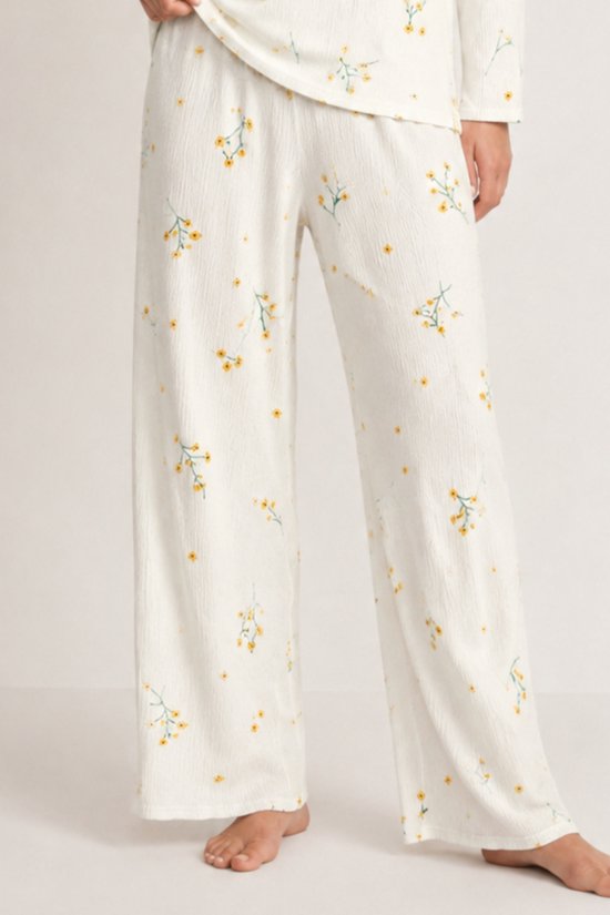 Close-up van de wijde broek van de ecru pyjamaset met een textuur en een patroon van kleine gele bloemen.