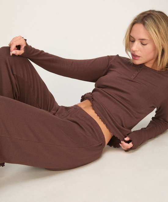 Liggend blond model draagt een bruine pyjamaset met geribbelde textuur en geschulpte zoomdetails.