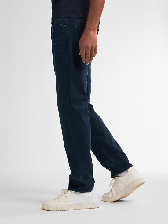 Een man draagt een donkerblauwe jeans met een regular tapered fit, met een witte sneaker.