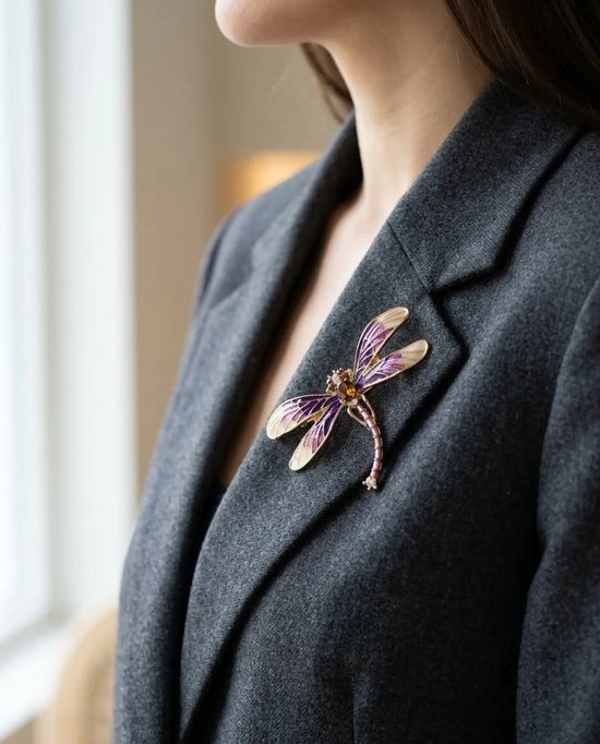 Gouden libellebroche met paars email, barnsteenkleurige steen en kristallen op een donkergrijze blazer.