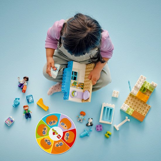 Meisje speelt met LEGO Duplo dokterscentrum. Losse onderdelen, figuren en draaischijf met emoties.