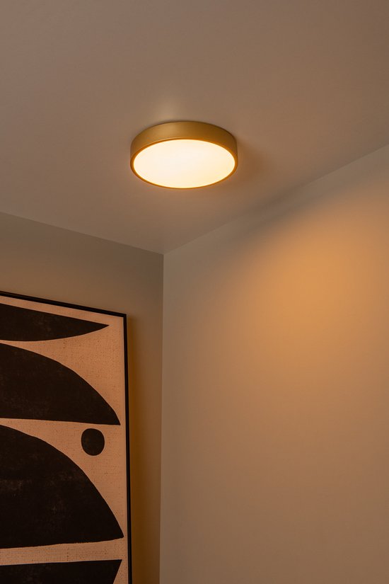 Moderne, ronde mat gouden plafondlamp in een slaapkamer, subtiel verlicht.