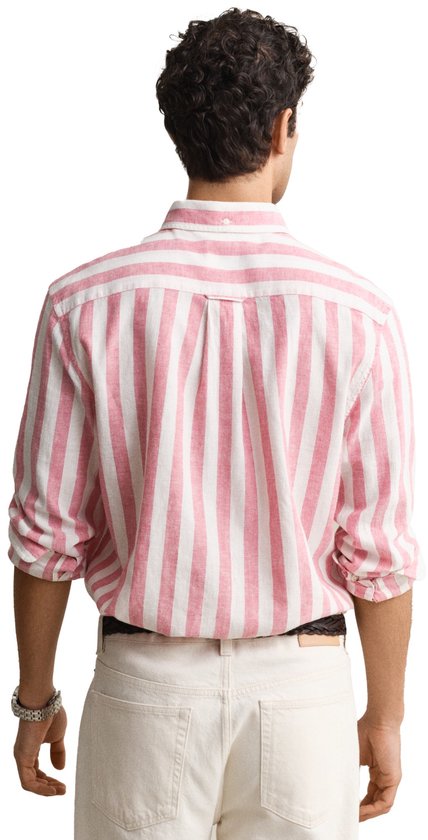 Man draagt een roze en wit gestreept katoen-linnen overhemd met opgerolde mouwen en beige broek.