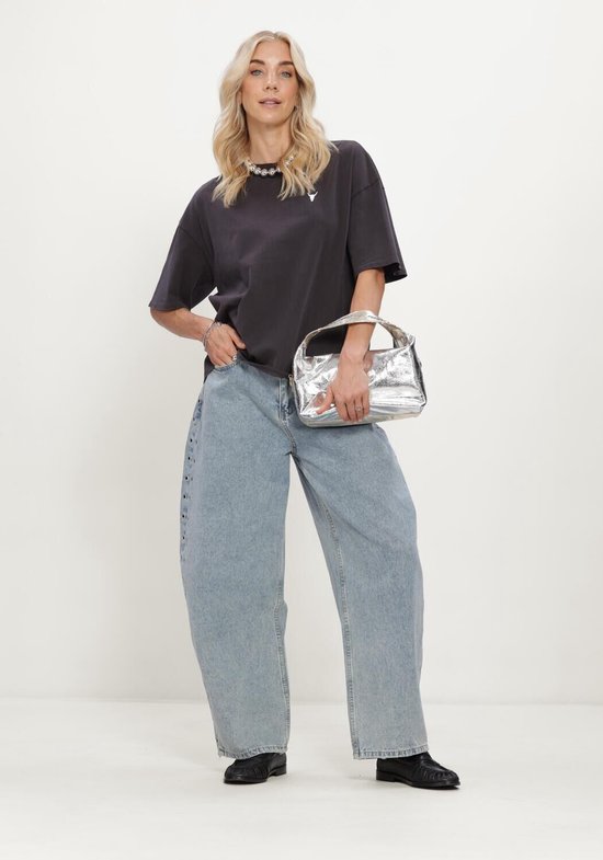 Model draagt oversized donkergrijs T-shirt met stierkop, wijde jeans en zilveren tas.