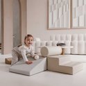 Een baby klimt op een beige en grijze speelset van schuimblokken in een woonkamer.