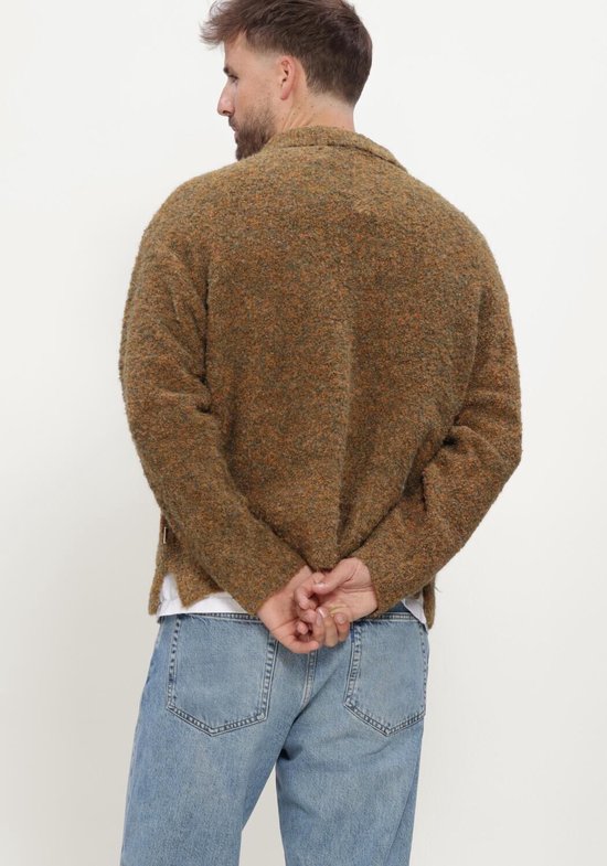 Achterkant van een man met handen achter zijn rug, in bruine gebreide polo en jeans.