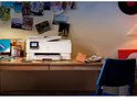 Witte HP Envy Photo printer op houten bureau in een kamer met fotowand en zachte verlichting.