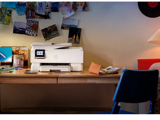 Witte HP Envy Photo printer op houten bureau in een kamer met fotowand en zachte verlichting.
