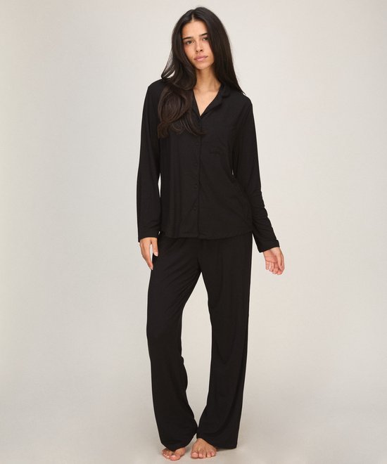 Model staat in een zwarte pyjamaset met kraag en losvallende broek.