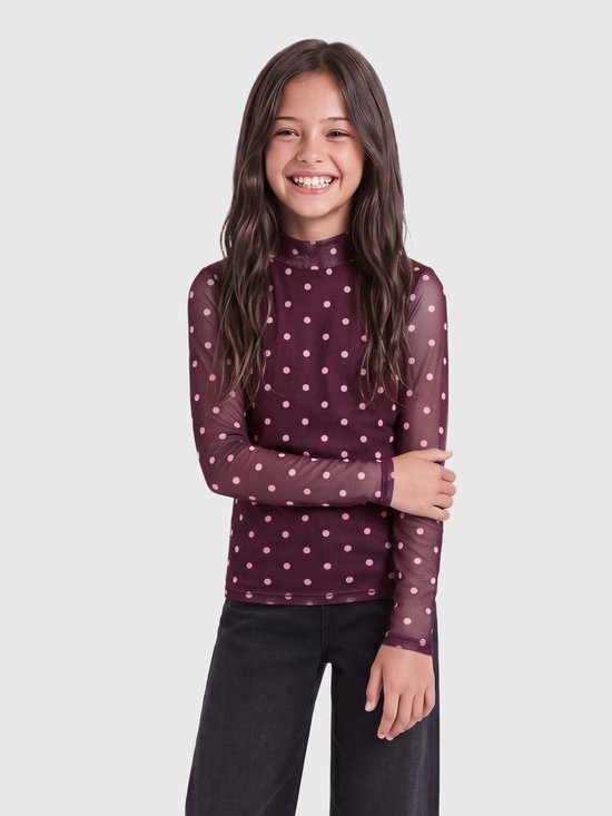 Lachend meisje draagt een bordeauxrode mesh top met lange mouwen en roze stippenpatroon.
