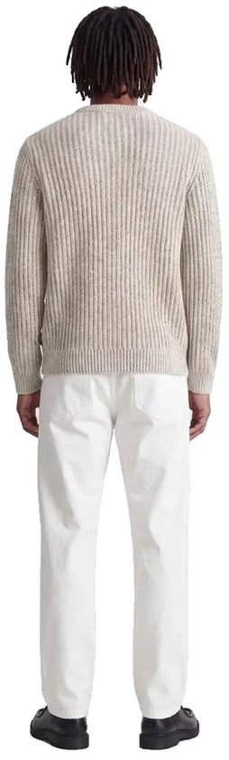 Model op de rug gezien in een beige trui met witte broek en zwarte schoenen.