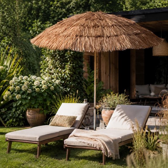 Raffia parasol bij twee ligbedden in een zonnige tuin met natuurlijke look.