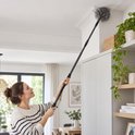 Vrouw gebruikt een grijze uitschuifbare ragebol om spinnenwebben van een hoog plafond te verwijderen.