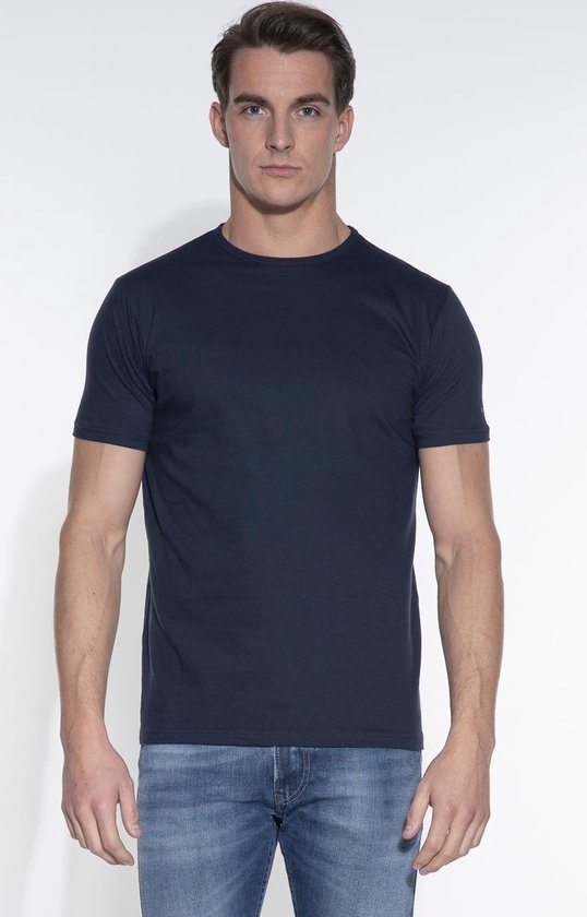 Model draagt een effen donkerblauw basic fit t-shirt met ronde hals en spijkerbroek.