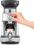 Zilverkleurige Sage koffiemolen, met een hand die de draaiknop voor maaltijd instelt.