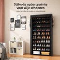 Een vrouw plaatst schoenen in een zwart schoenenrek met 10 lagen, naast een zithoek.