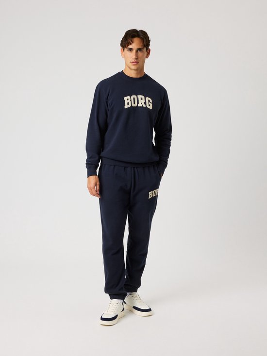 Man draagt een donkerblauwe sweater met beige 'BORG' opdruk en bijpassende joggingbroek.