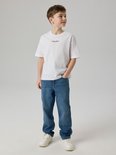 Jongen draagt een witte t-shirt met 'Studio edition' tekst en blauwe jeans.