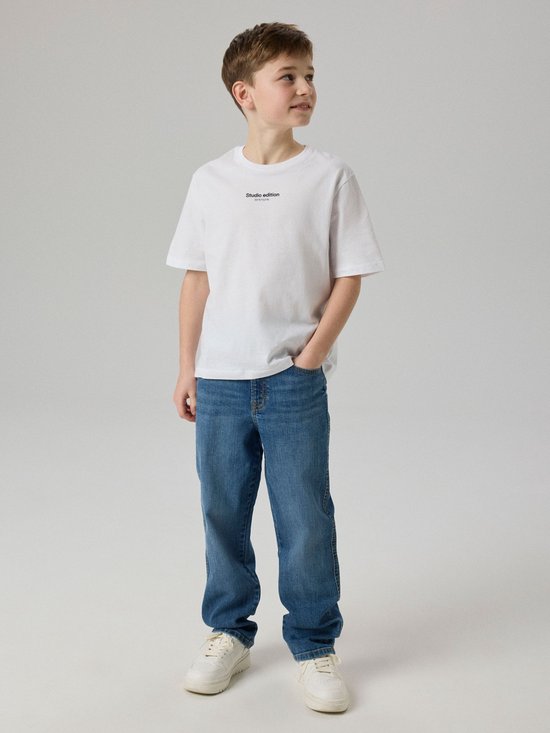 Jongen draagt een witte t-shirt met 'Studio edition' tekst en blauwe jeans.
