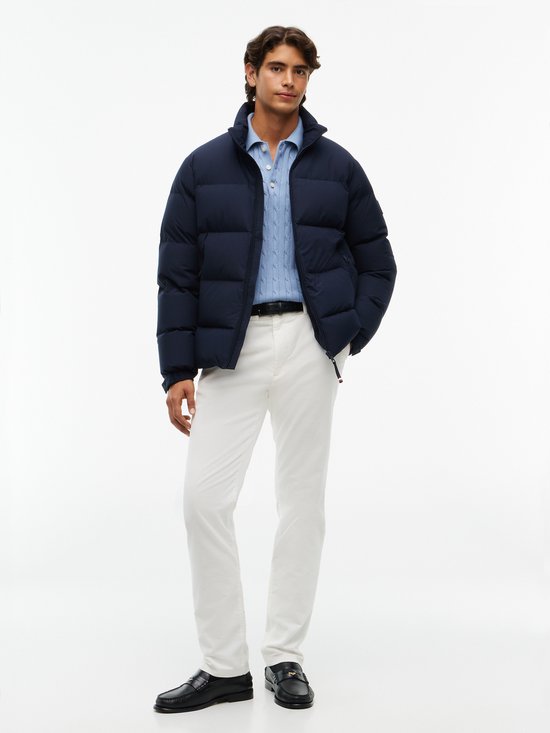 Man draagt een donkerblauwe gewatteerde jas over een lichtblauwe kabeltrui en witte broek.