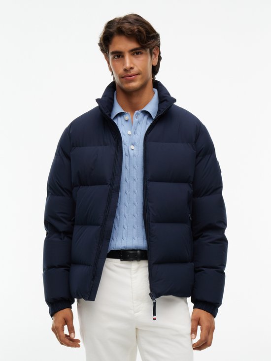 Man in een donkerblauwe gewatteerde jas met ritssluiting, gecombineerd met een lichtblauwe kabeltrui.