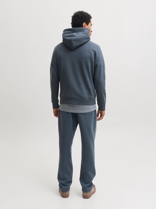 Man in een donkerblauwe joggingbroek met trekkoord en een bijpassende hoodie, sneaker.