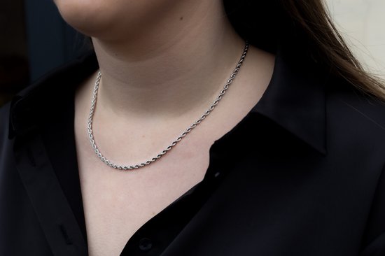 Een zilverkleurige, gedraaide touwketting gedragen rond de nek van een vrouw over een zwart overhemd met opengewerkte kraag.