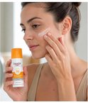 Een vrouw brengt Eucerin zonnebrandcrème met SPF 50 aan op haar gezicht. Ze houdt de fles in haar hand.