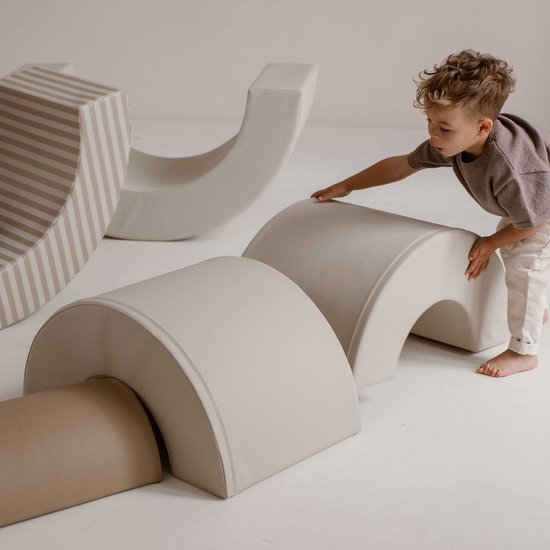 Jongen speelt met beige en witte schuimblokken, een gebogen blok is beige-wit gestreept.