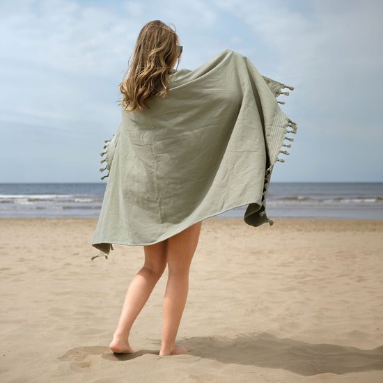 Vrouw op het strand met een groene hamamdoek omgeslagen, met de rug naar de camera.
