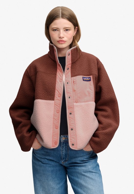 Model draagt bruine, roze en lichtroze fleece jas met hoge kraag.