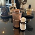 Koperkleurige, geribbelde Aroma diffuser met een flesje geurolie op een spiegelende tafel.