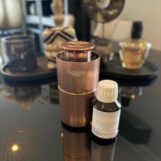 Koperkleurige, geribbelde Aroma diffuser met een flesje geurolie op een spiegelende tafel.