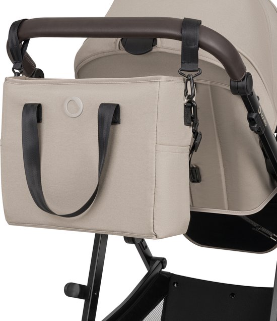 Beige verzorgingstas aan de duwstang van een kinderwagen.