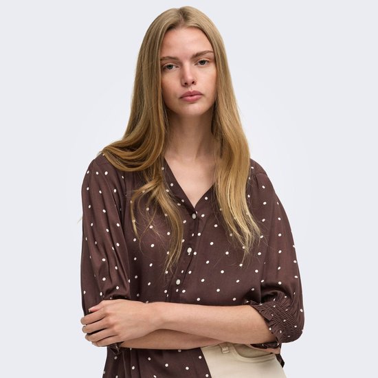 Bruine blouse met witte stippen, driekwart mouwen, gedragen door een model.