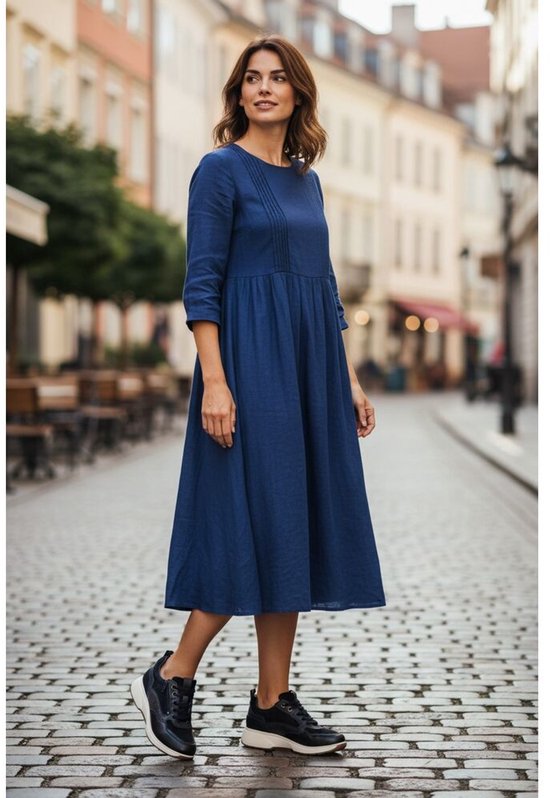 Vrouw met blauwe jurk en donkerblauwe sneakers in een straatbeeld.