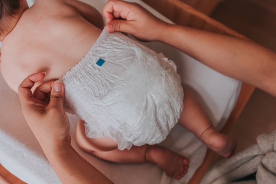 Een baby op de rug met een 'Woosh' luierbroekje. De luier wordt vastgehouden door twee handen.