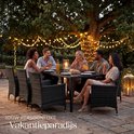 Een groep van vijf vrienden geniet van een etentje aan een zwarte wicker tuinset onder een boom met kerstverlichting.