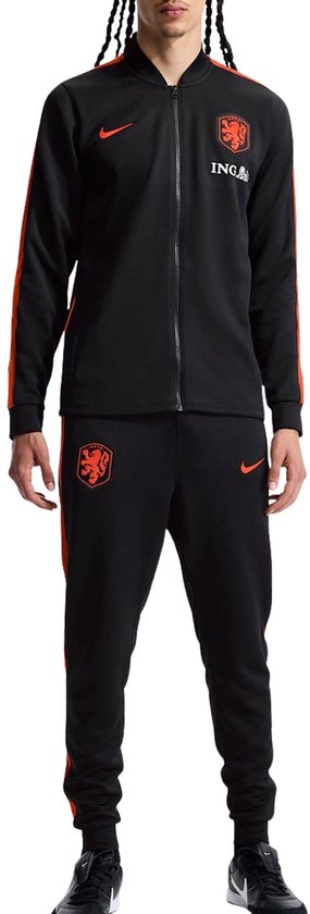 Man in een zwart trainingspak van Nike met oranje strepen en logo's.