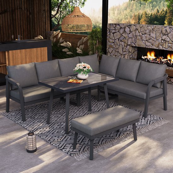 Ensemble de salon gris avec table en verre et banc sur un tapis géométrique noir et blanc dans un jardin.