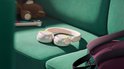 Roze en witte Philips koptelefoon met verlichte oorschelpen, liggend op een groene bank naast een teddybeer.