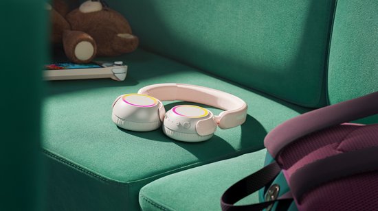 Roze en witte Philips koptelefoon met verlichte oorschelpen, liggend op een groene bank naast een teddybeer.