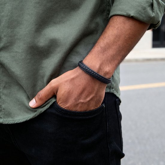 Zwarte gevlochten leren armband om de pols van een man met zijn hand in zijn zak.