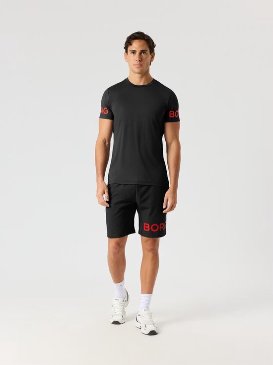Man in zwart sportshirt met rode Björn Borg letters op de mouwen en bijpassende zwarte sportshort met rode letters.
