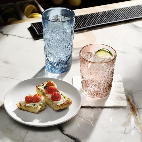 Blush rosé en blauw gedetailleerd kristalglas op een marmeren bar met drankjes.