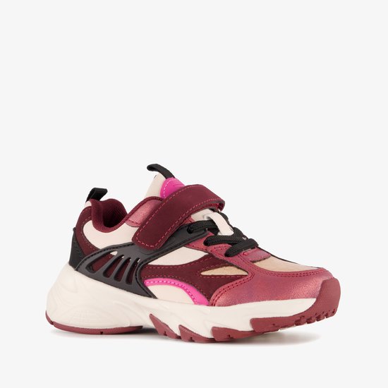 Zij-aanzicht van een rode en paarse kindersneaker met klittenbandsluiting, witte zool en zwarte accenten.